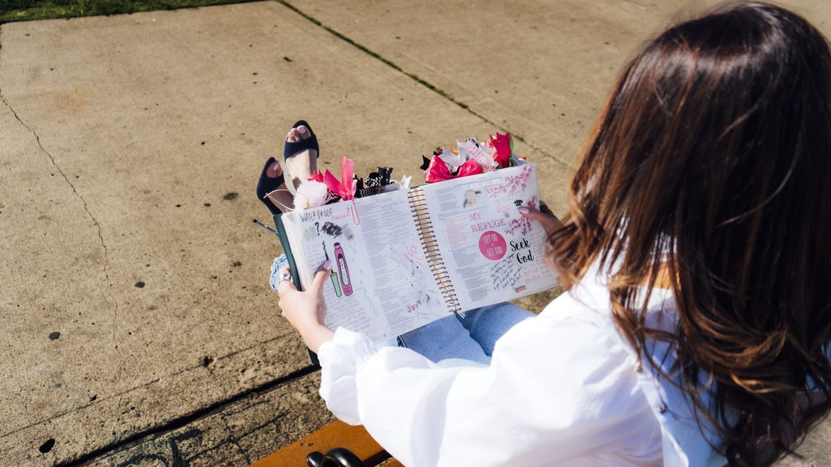 Vista sobre el hombro de una Biblia de journaling abierta, marcada con stickers, cinta y separadores de colores.