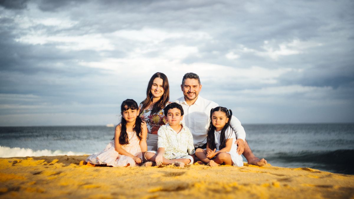 Michelle y Efrén Ruiz sentados en la arena al atardecer con sus tres hijos.