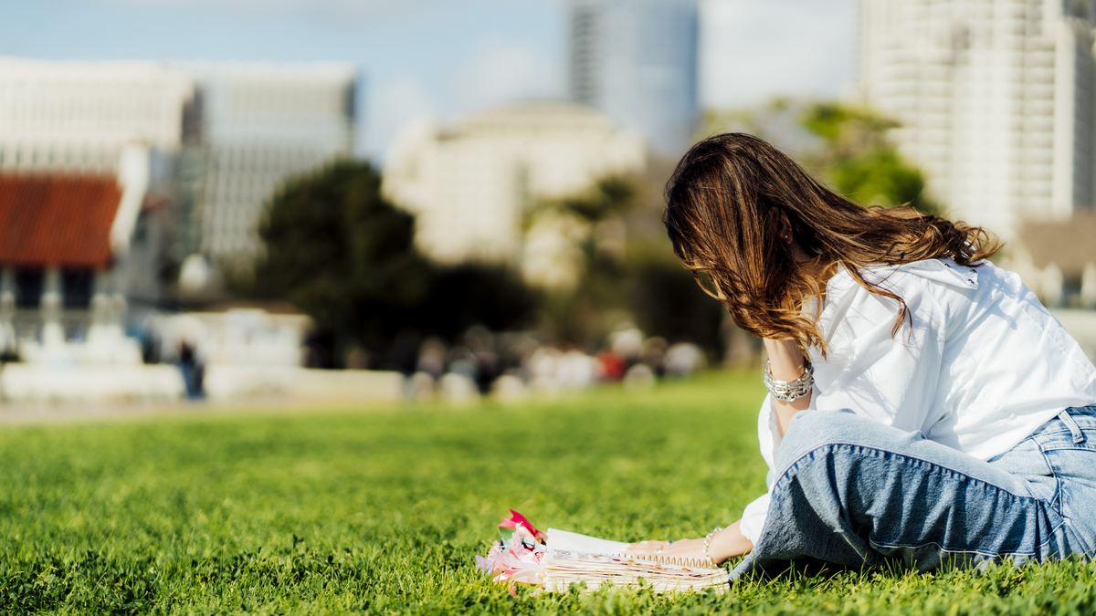 Michelle Ruiz inclinada sobre el pasto, escribiendo en su Biblia.