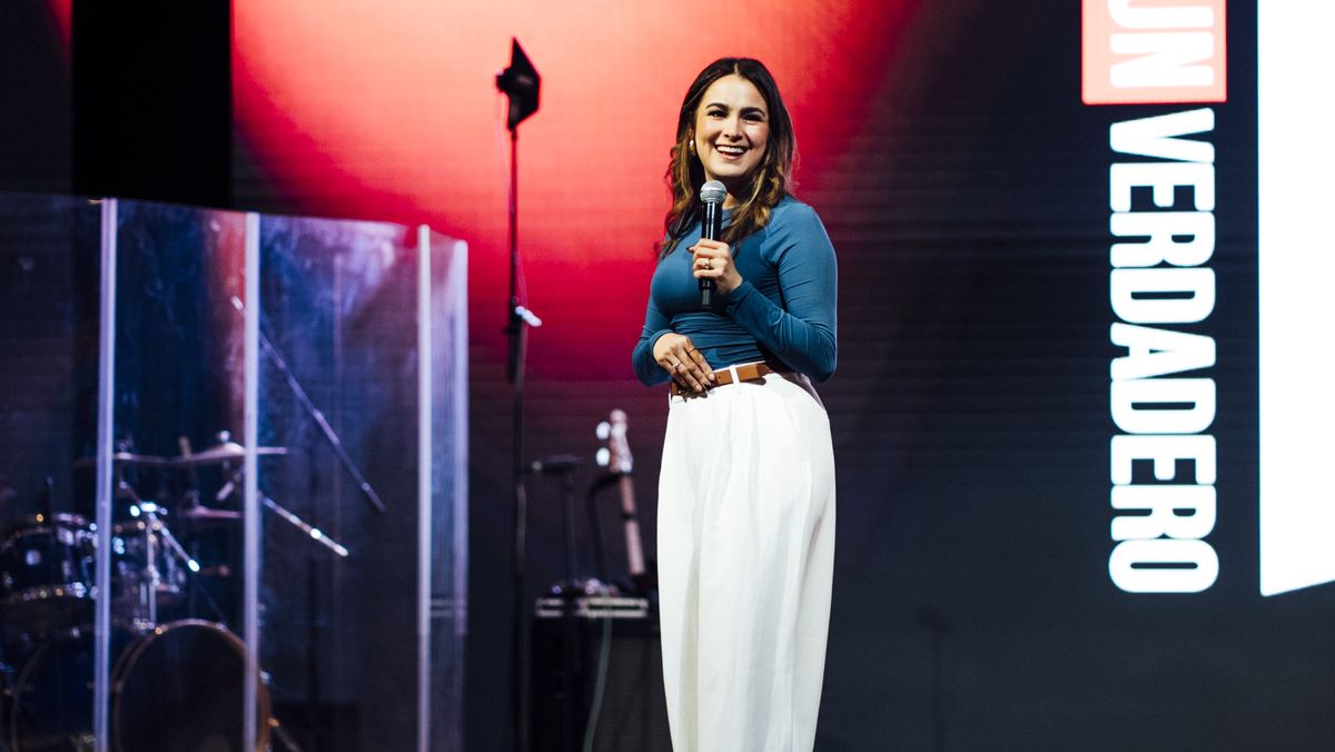 Michelle Ruiz con micrófono en el escenario, ante una pantalla que dice «Un verdadero».